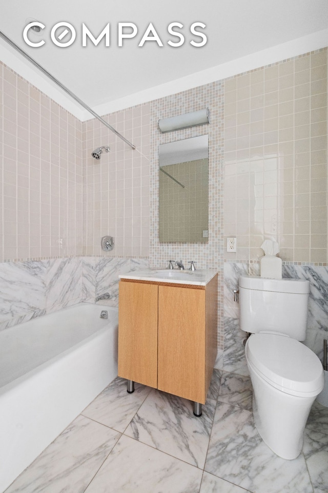 full bathroom featuring tile walls, marble finish flooring, washtub / shower combination, toilet, and vanity