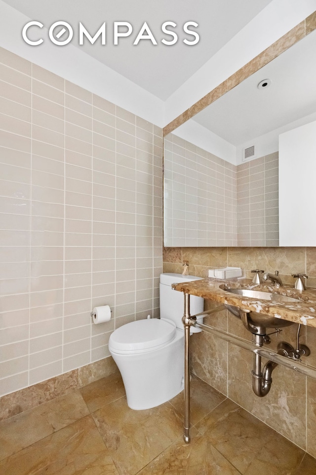 bathroom with toilet, tile walls, a sink, backsplash, and tile patterned floors