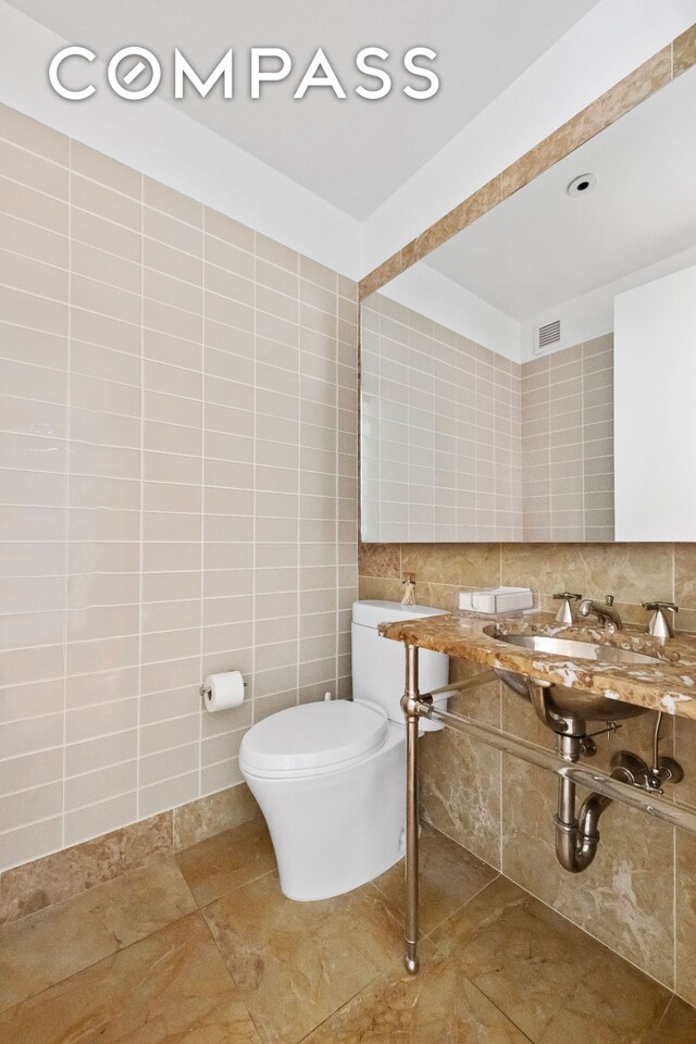 255 E 74th St Unit 14C, New York City, NY 10021 - bathroom featuring toilet, tile walls, decorative backsplash, and tile patterned flooring