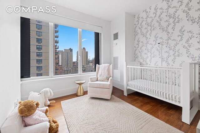255 E 74th St Unit 14C, New York City, NY 10021 - bedroom featuring wood finished floors, a view of skyline, a crib, and baseboards