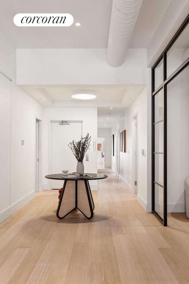 hallway featuring baseboards, a raised ceiling, and light wood-style floors
