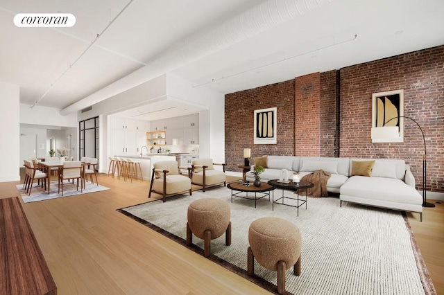 living room featuring visible vents, brick wall, and light wood-style floors