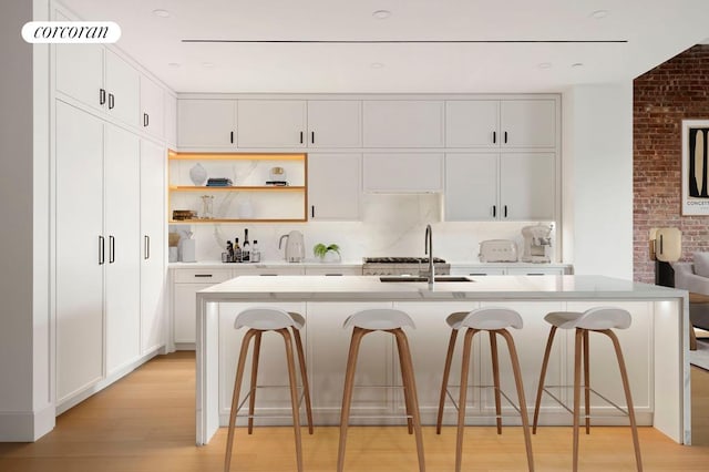 kitchen with light wood-style floors, white cabinets, a breakfast bar, light countertops, and a sink