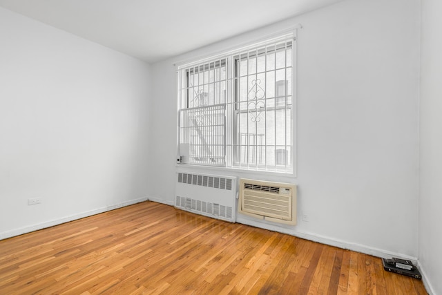 empty room with radiator, wood finished floors, baseboards, and a wall unit AC