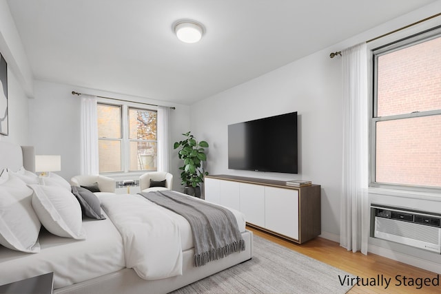 bedroom featuring light wood-style floors, baseboards, and an AC wall unit