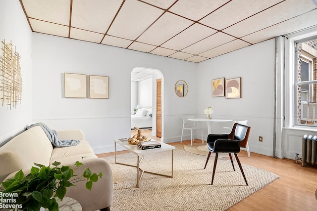 living area featuring arched walkways, radiator heating unit, wood finished floors, and a paneled ceiling