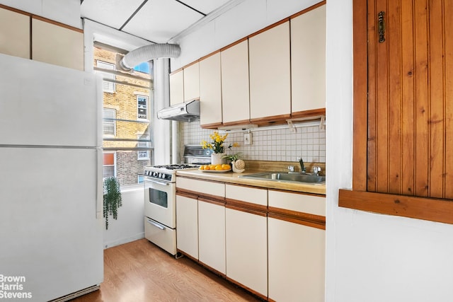 kitchen with white appliances, a sink, tasteful backsplash, light wood finished floors, and under cabinet range hood