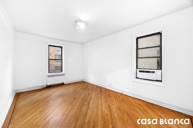 empty room with baseboards, wood finished floors, radiator, and cooling unit