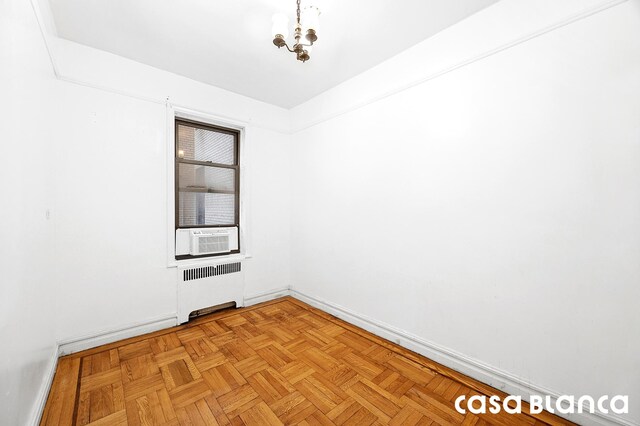 unfurnished room featuring baseboards, a notable chandelier, radiator heating unit, and cooling unit