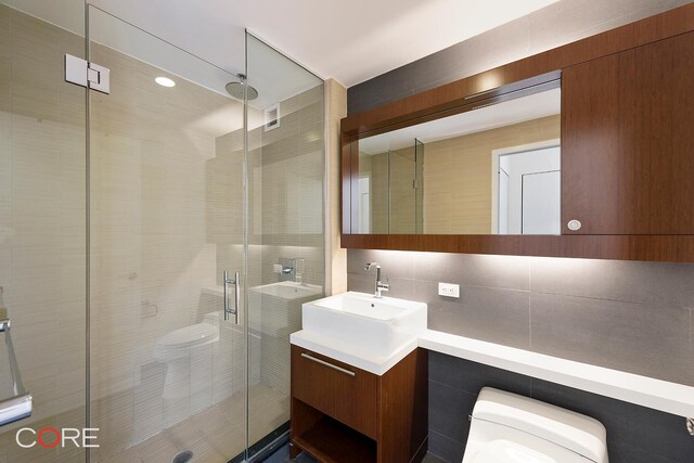 305 W 16th St Unit 4E, New York City, NY 10011 - bathroom featuring toilet, tile walls, vanity, a stall shower, and tasteful backsplash