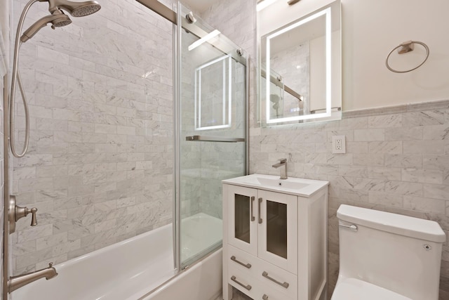 bathroom with shower / bath combination with glass door, toilet, tile walls, a wainscoted wall, and vanity