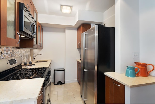 kitchen with appliances with stainless steel finishes, decorative backsplash, light countertops, glass insert cabinets, and a sink