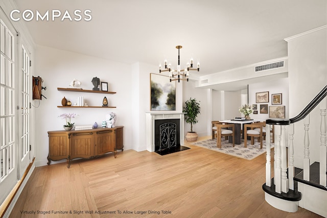 interior space featuring a fireplace with flush hearth, visible vents, a notable chandelier, and light wood-style floors