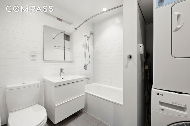 221 E 50th St Unit 6D/7D, New York City, NY 10022 - bathroom featuring stacked washer / drying machine, vanity, shower / bathtub combination, toilet, and tile walls