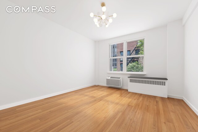 221 E 50th St Unit 6D/7D, New York City, NY 10022 - unfurnished room featuring radiator heating unit, a chandelier, light wood-style flooring, a wall mounted AC, and baseboards