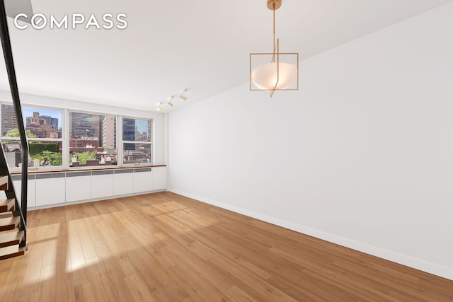 unfurnished dining area with track lighting, a view of city, baseboards, and light wood finished floors