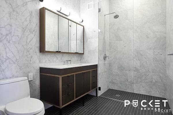 184 Kent Ave Unit C-614, New York City, NY 11249 - bathroom featuring toilet, vanity, tiled shower, tile walls, and tile patterned floors