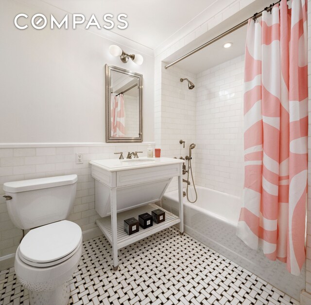 bathroom featuring toilet, shower / bath combo, vanity, wainscoting, and tile walls