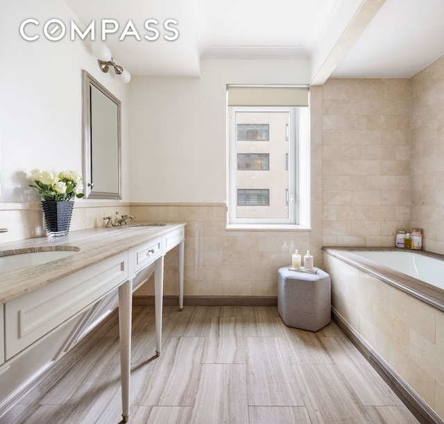 bathroom featuring tile walls, wood finished floors, tiled bath, double vanity, and crown molding