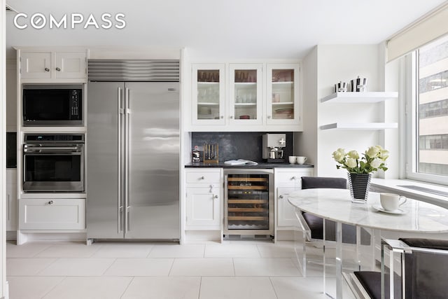 kitchen with built in appliances, beverage cooler, white cabinetry, glass insert cabinets, and backsplash
