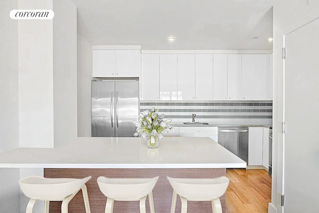 kitchen with stainless steel appliances, a sink, white cabinets, a kitchen breakfast bar, and light countertops