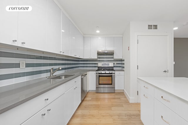 kitchen featuring appliances with stainless steel finishes, a sink, white cabinetry, under cabinet range hood, and light wood-style floors