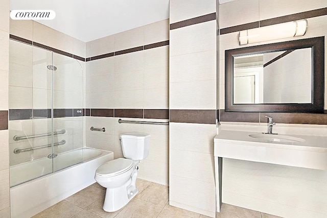 bathroom with toilet, combined bath / shower with glass door, tile patterned floors, tile walls, and vanity