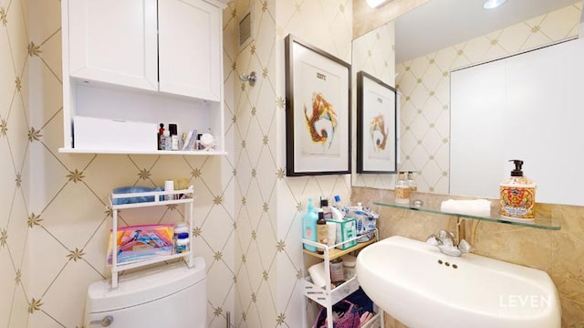 bathroom with a sink, toilet, and tile walls