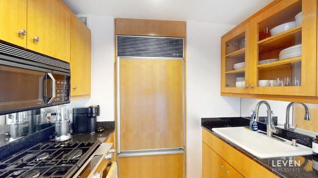kitchen featuring paneled built in fridge, glass insert cabinets, black microwave, and a sink