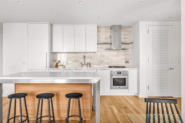 kitchen featuring wall chimney range hood, a kitchen bar, appliances with stainless steel finishes, a sink, and light countertops