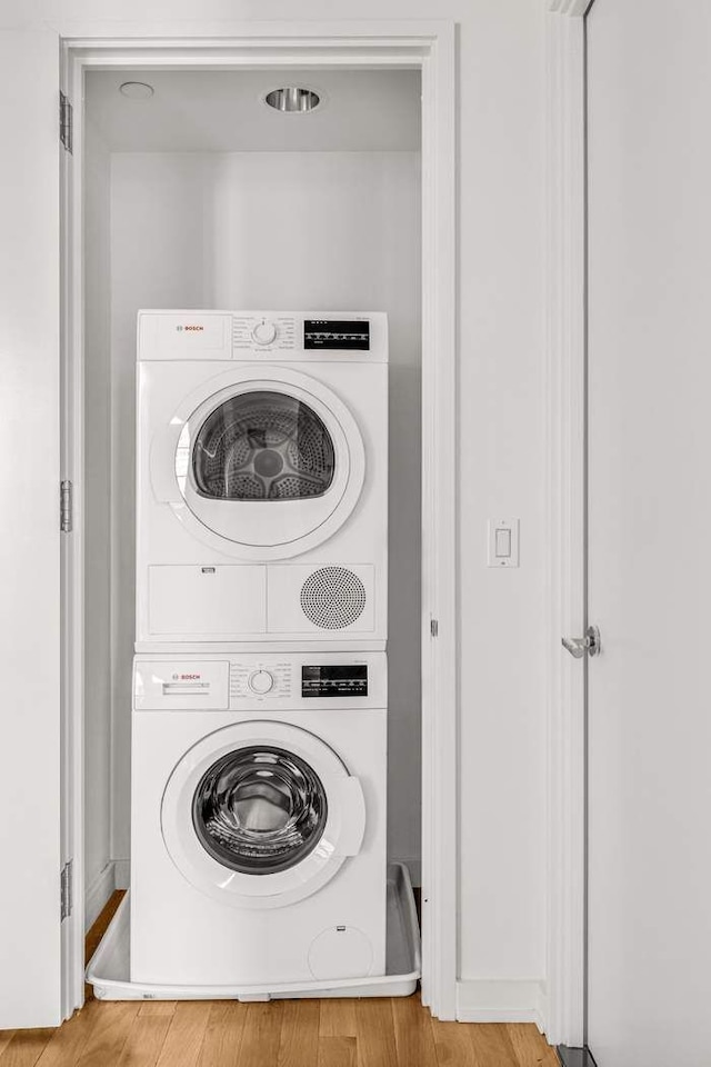 laundry area featuring baseboards, stacked washer and clothes dryer, wood finished floors, and laundry area
