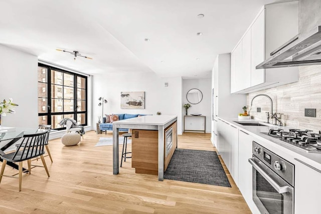 kitchen with oven, a sink, light wood-style flooring, gas stovetop, and backsplash