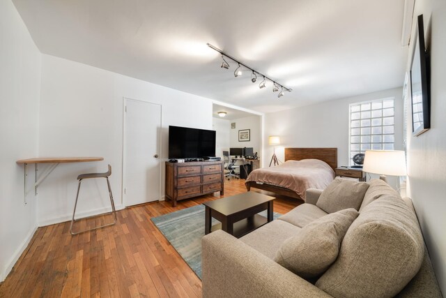 bedroom with hardwood / wood-style floors, rail lighting, and baseboards