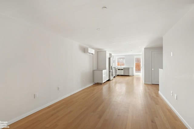 unfurnished living room featuring baseboards, light wood-style floors, and a wall mounted AC
