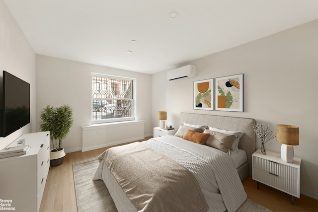 bedroom featuring a wall mounted air conditioner, baseboards, and light wood-type flooring