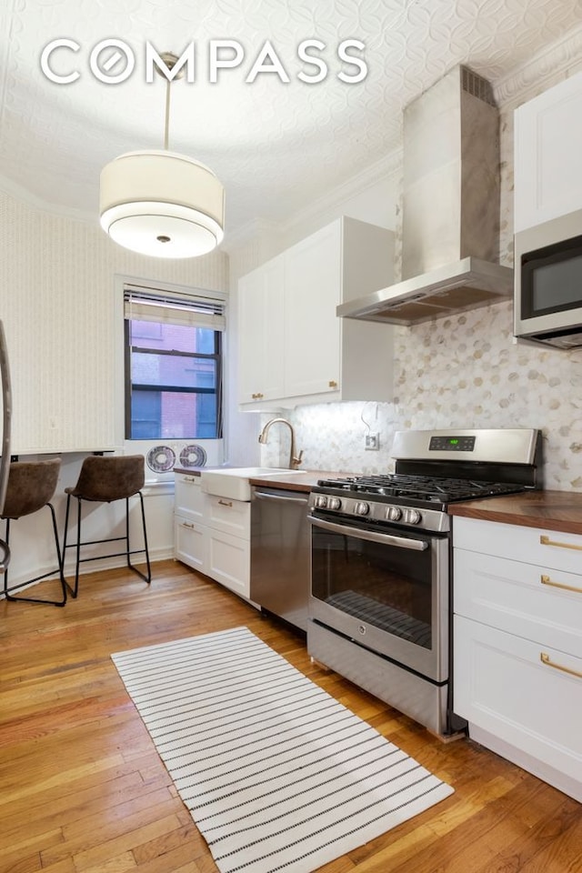 31 Tiemann Pl Unit 37, New York City, NY 10027 - kitchen with appliances with stainless steel finishes, wall chimney range hood, ornamental molding, a sink, and white cabinets