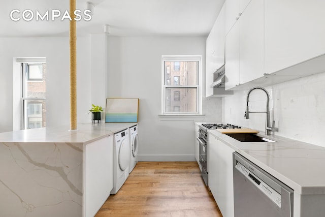 kitchen with light wood-type flooring, appliances with stainless steel finishes, a peninsula, under cabinet range hood, and washing machine and dryer