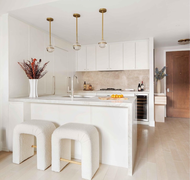 kitchen with wine cooler, a sink, light countertops, white cabinetry, and tasteful backsplash