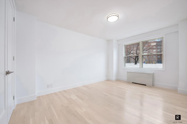 unfurnished room featuring wood finished floors, baseboards, and radiator