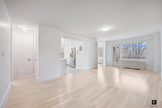 unfurnished living room featuring baseboards, radiator heating unit, and light wood finished floors
