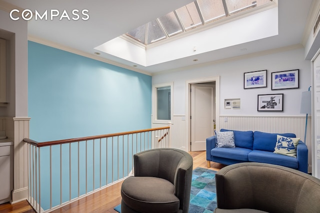 living area featuring a wainscoted wall, wood finished floors, ornamental molding, and a skylight