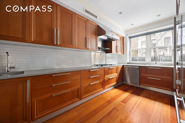 217 W 22nd St, New York City, NY 10011 - kitchen featuring dishwasher, brown cabinetry, under cabinet range hood, light wood-style flooring, and crown molding