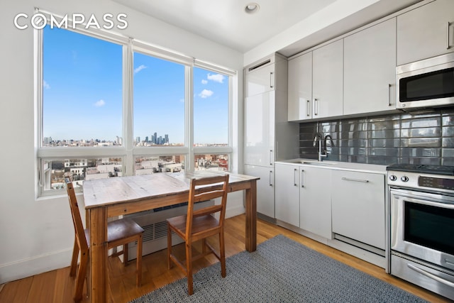 kitchen with appliances with stainless steel finishes, a sink, light countertops, light wood-type flooring, and backsplash