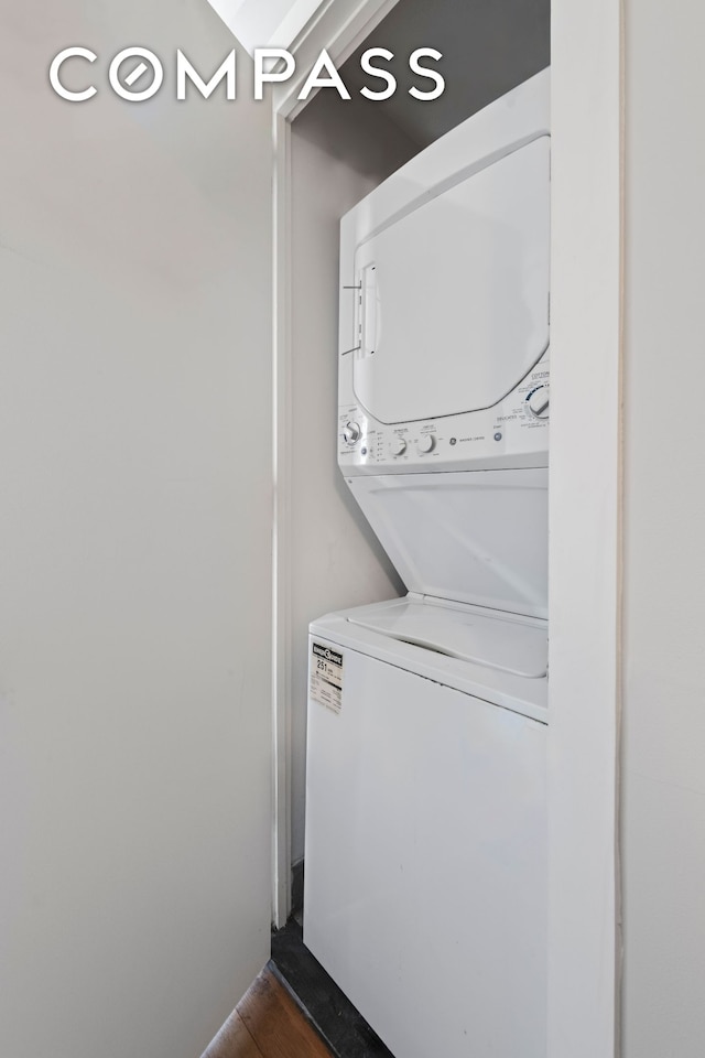clothes washing area featuring stacked washer / drying machine, dark wood-style floors, and laundry area