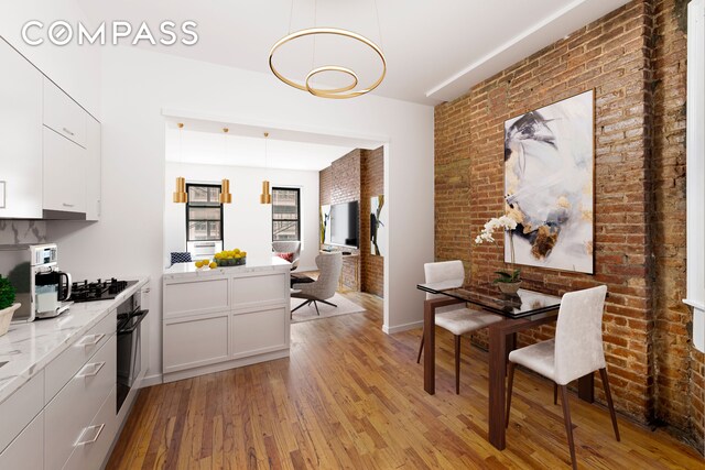 433 W 54th St Unit 1, New York City, NY 10019 - dining room featuring brick wall, an inviting chandelier, and light wood-type flooring