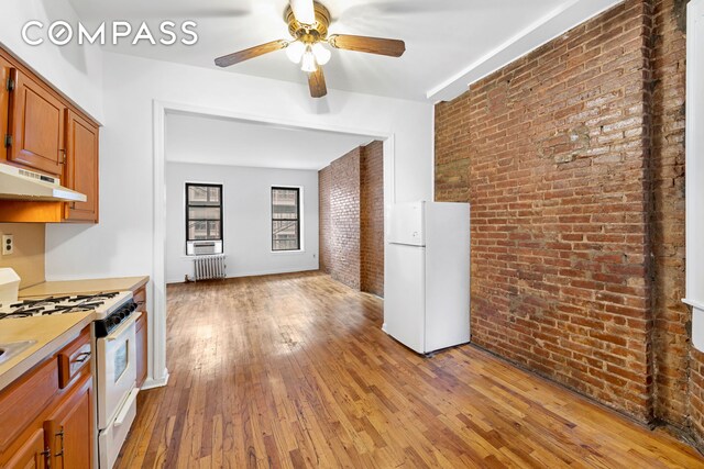 433 W 54th St Unit 1, New York City, NY 10019 - kitchen featuring brick wall, ceiling fan, white appliances, radiator heating unit, and light wood-style flooring