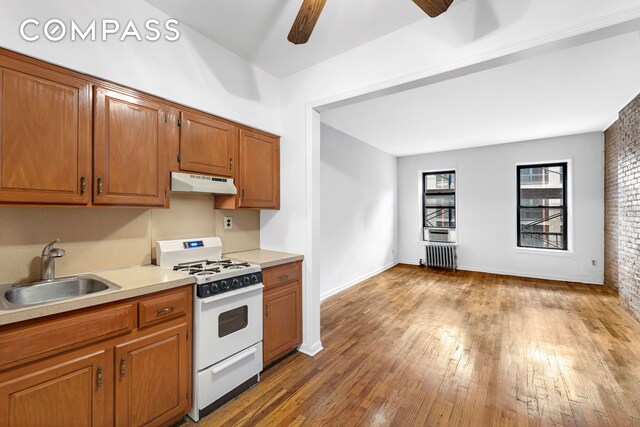 433 W 54th St Unit 1, New York City, NY 10019 - kitchen featuring a sink, a ceiling fan, under cabinet range hood, white gas range, and radiator heating unit