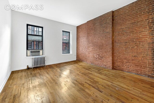 433 W 54th St Unit 1, New York City, NY 10019 - spare room featuring baseboards, brick wall, hardwood / wood-style flooring, radiator, and cooling unit