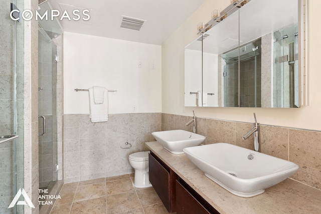 125 W 21st St Unit 12A, New York City, NY 10011 - bathroom featuring tile walls, a shower stall, toilet, double vanity, and a wainscoted wall
