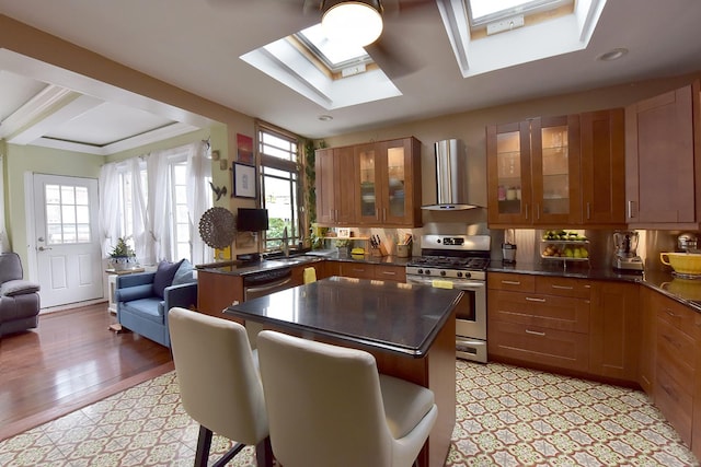 34 Fort Charles Place, New York City, NY 10463 - kitchen featuring wall chimney exhaust hood, appliances with stainless steel finishes, dark countertops, a skylight, and brown cabinets